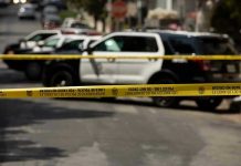 Police tape blocking street with patrol cars.