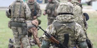 Soldiers in camouflage gear gathered on grass field.
