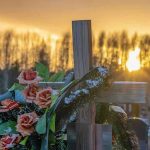 Cross with flowers at cemetery during sunset.