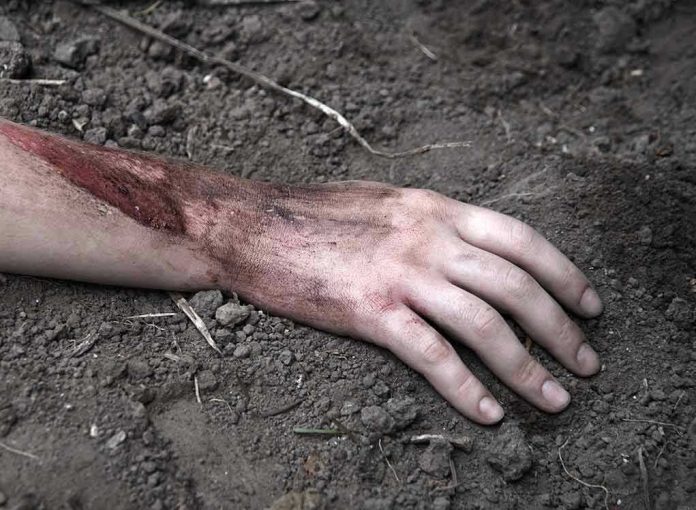Injured arm partially buried in dirt.