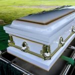 White casket on a lowering device at gravesite.