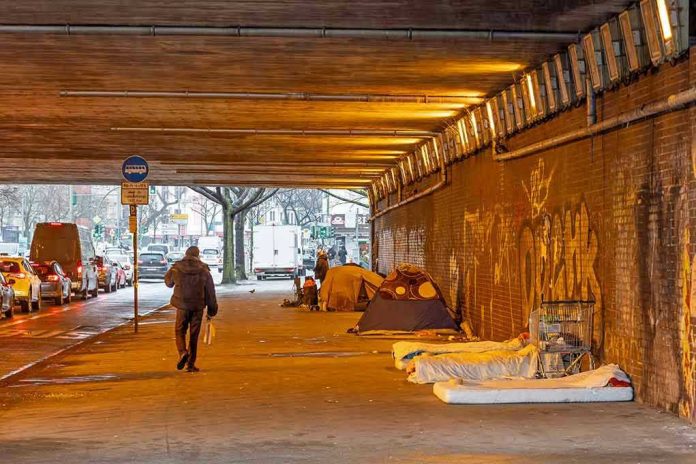 People walk under a bridge with homeless encampment.