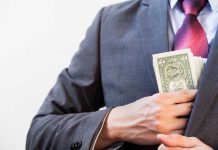 Person in suit putting dollars in jacket pocket.