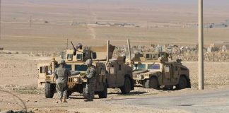 War Hero ARRESTED — Murder Charges STUN Soldiers standing near armored vehicles in desert terrain.