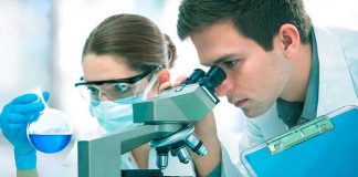 Two scientists conducting an experiment in a laboratory, one looking through a microscope and the other holding a flask with blue liquid