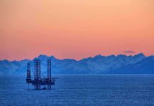 IRAN’S 6,000 MINES CHOKE Global Oil Supply An oil rig in the ocean with a backdrop of mountains during sunset
