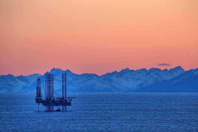 An oil rig in the ocean with a backdrop of mountains during sunset