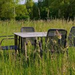 A rustic table and chairs set in a grassy field surrounded by nature