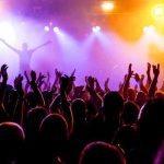 Crowd at a concert with raised hands and colorful stage lights