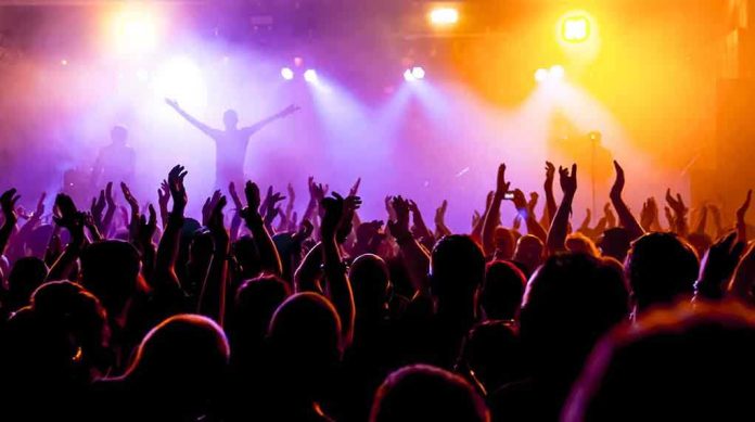 Crowd at a concert with raised hands and colorful stage lights