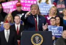 Person speaking at rally with crowd behind podium