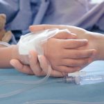 Shock: UK Quietly Rations Life-Saving Drugs Childs hand with IV, held by adult.