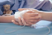 Shock: UK Quietly Rations Life-Saving Drugs Childs hand with IV, held by adult.