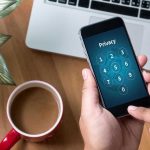 Banking Scandal: Threats Hidden in Payment Messages Typing privacy passcode on smartphone near laptop and coffee.