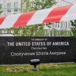 Kari Lake’s SHOCKING Diplomatic Twist U.S. Embassy sign behind red-and-white caution tape.