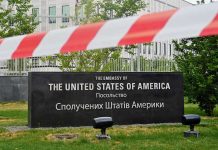 U.S. Embassy sign behind red-and-white caution tape.