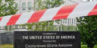 Kari Lake’s SHOCKING Diplomatic Twist U.S. Embassy sign behind red-and-white caution tape.