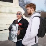 Two individuals at a protest, one holding a portrait of a woman