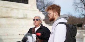 Two individuals at a protest, one holding a portrait of a woman