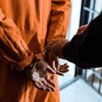 Morality Police Put Pain On Display Handcuffed person in orange jumpsuit being escorted.