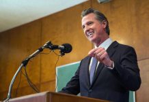 Pay Grab Frenzy Hits California Schools A man in a suit delivering a speech at a podium with microphones