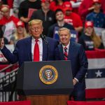 Trump’s Roast Turns Hostile: Press Left Shaken two men at a podium during a large indoor rally