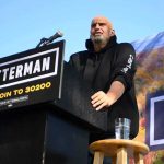 Communism Alarm Ignites Democratic Firestorm Speaker at outdoor rally standing at podium with microphone