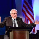 Insider Bombshell Hits Sanders elderly man speaking at a podium with arms outstretched
