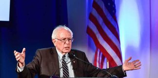 elderly man speaking at a podium with arms outstretched