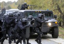 Tactical police team advances from armored vehicle with shields and rifles