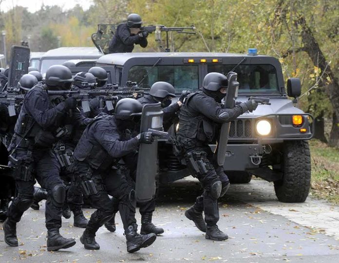 shutterstock_346794716 Tactical police team advances from armored vehicle with shields and rifles
