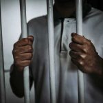Person gripping prison bars with both hands