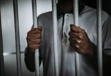 Person gripping prison bars with both hands