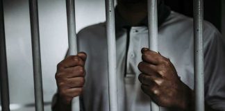 Person gripping prison bars with both hands