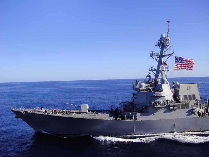 shutterstock_1133692649 Naval destroyer sailing on open sea with flag flying