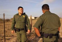 Two uniformed officers walking along a rural fence line