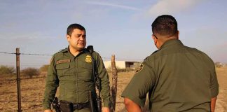 Two uniformed officers walking along a rural fence line
