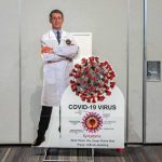 Shocking Pick to Succeed Fauci Cardboard cutout of doctor with COVID-19 virus info display