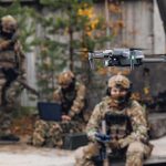 Marines Can Now Strike Targets 20 Kilometers Away With New FPV Drones Quadcopter drone flying near camouflaged soldiers outdoors