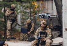 Quadcopter drone flying near camouflaged soldiers outdoors