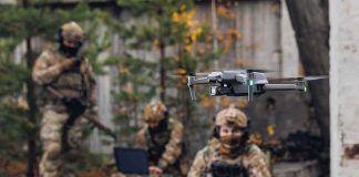 Quadcopter drone flying near camouflaged soldiers outdoors