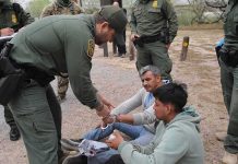 law enforcement officer handcuffing two seated men outdoors