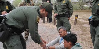 Illegal Caught by His Own Mugshot After Lying to ICE law enforcement officer handcuffing two seated men outdoors