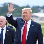 Donald Trump waves while walking outdoors with security nearby