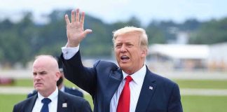 Donald Trump waves while walking outdoors with security nearby