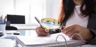 Person using a magnifying glass to review documents in a binder