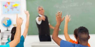 Students raising hands in a classroom while teacher points