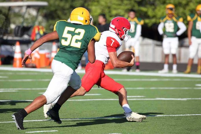 Football player in red runs with the ball as defender in green attempts a tackle