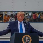 Donald Trump speaks at a podium with arms outstretched