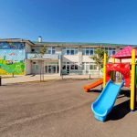 22 Children at Center of Paris Nursery Horror Playground with colorful slide in front of a school building